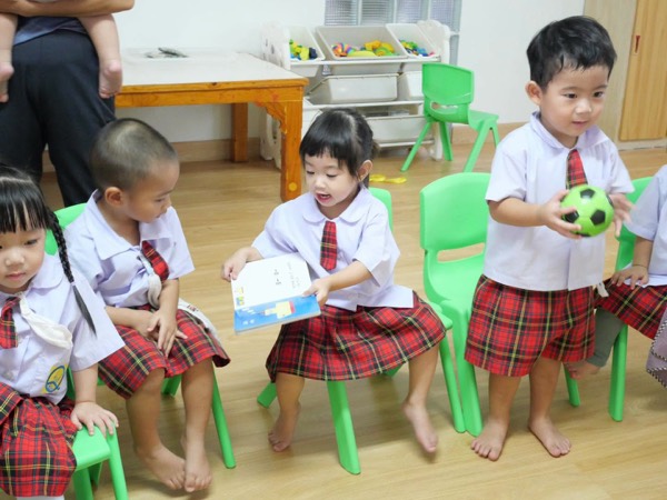 Children on chairs, one holding a book and another a ball
