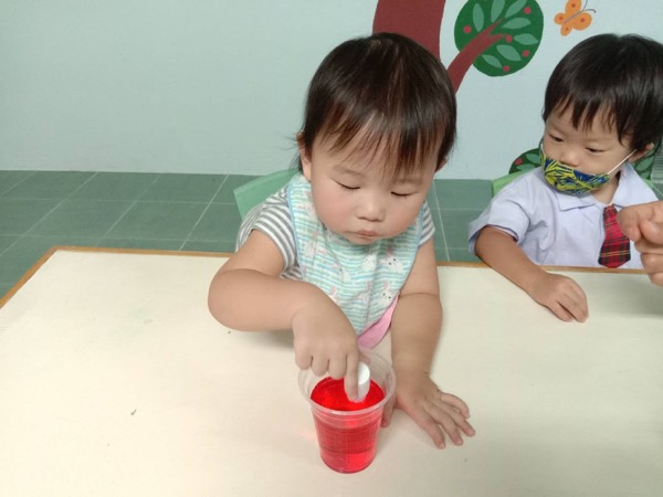 A small child stirring red jelly in a plastic cup at the table