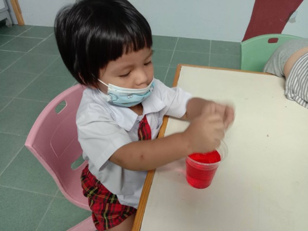 A boy sitting and stirring the red jelly in his own cup