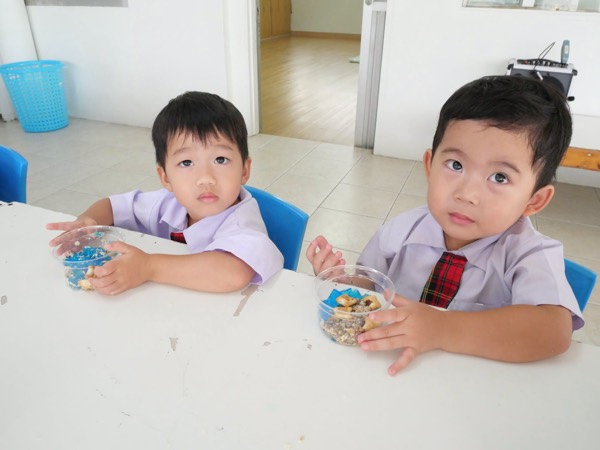 Two boys holding the dessert cups they made, at a long table
