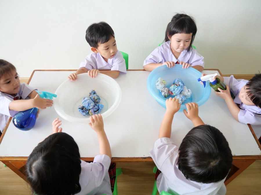 真上から見た、テーブルを囲んで二つの洗面器の布に色を吹きかける子どもたち