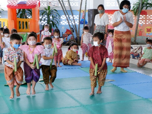 Children in Thai dress holding banana-leaf krathong, lined up in the hall