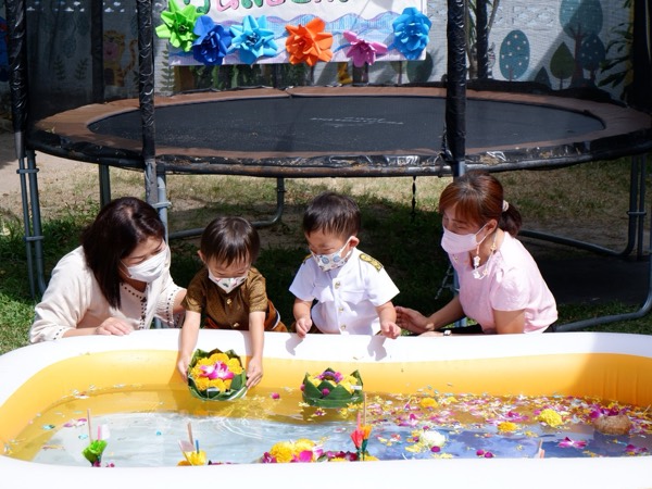 Two teachers helping small children float their krathong