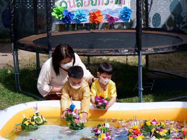 Two boys in gold Thai dress floating their krathong on the pool