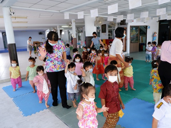 Children in Thai dress walking in a line through the covered hall