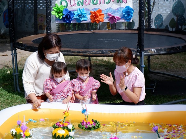 A teacher and two children in Thai dress floating a krathong on the pool