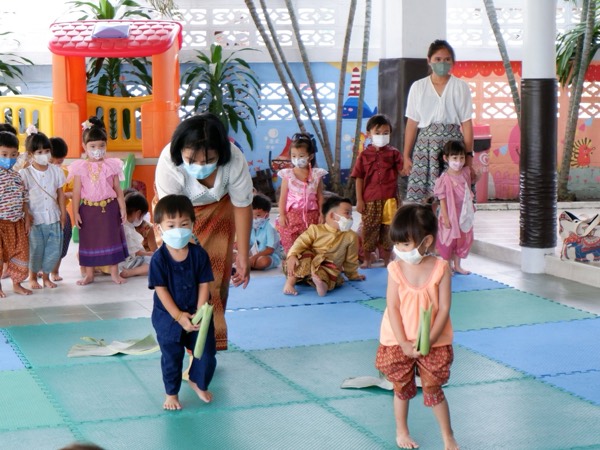 Children in Thai dress carrying their krathong across the hall