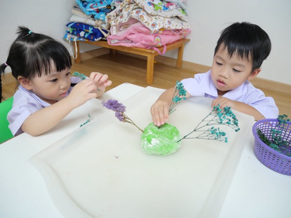 Two children planting dried stems into a lump of dough together
