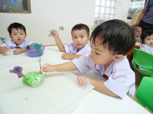 Children planting dried flowers into green dough at the table
