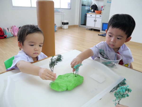 Two children planting little trees onto their green dough island