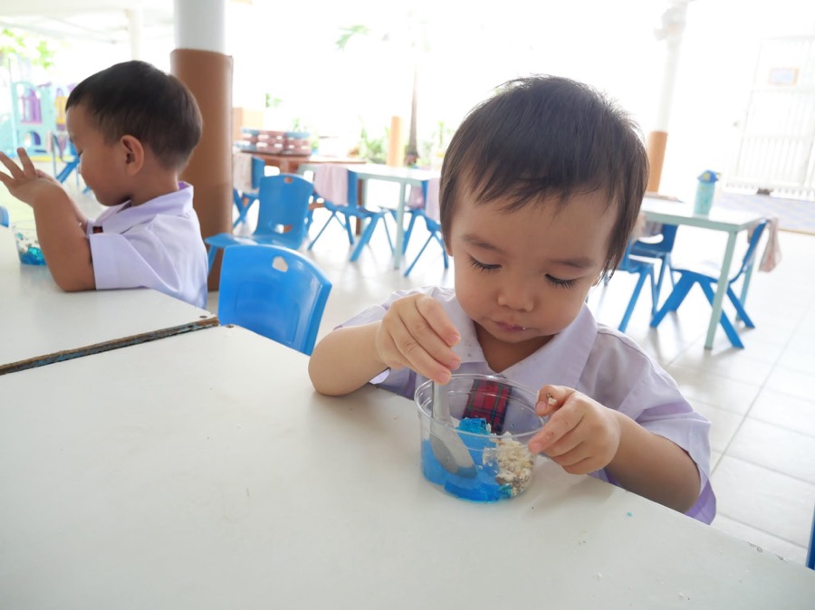 屋根のある広場のテーブルでおやつを食べる子どもたち。後ろには遊具