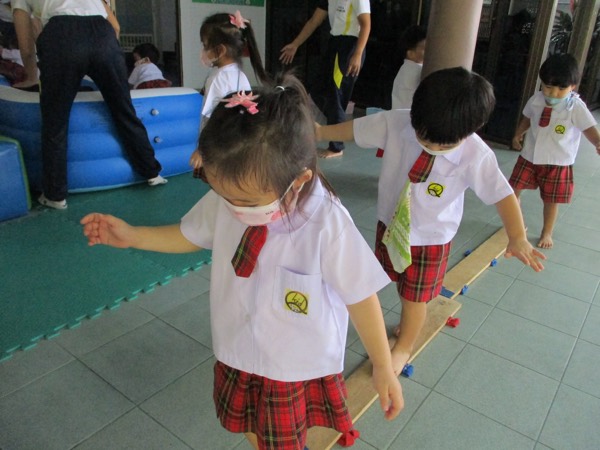 Children walking the length of a balance beam laid on the mats