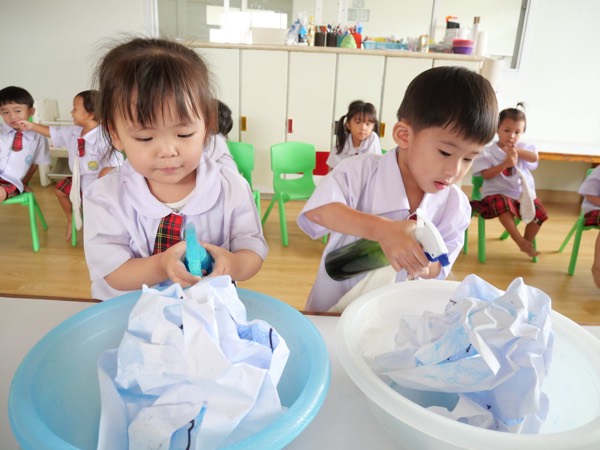 Two children with spray bottles, each colouring the cloth in their own basin