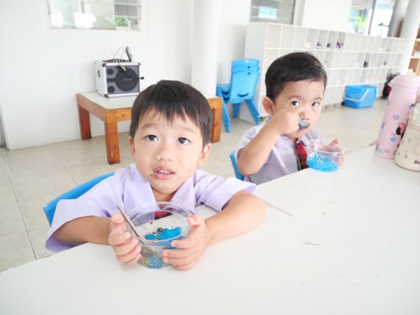 Two children eating the blue jelly dessert they made, from plastic cups