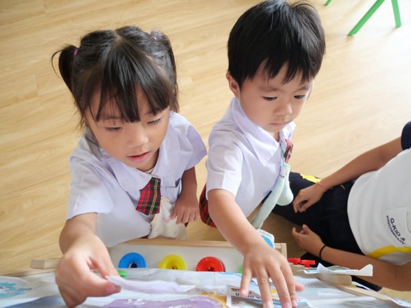 Two children leaning over a map on the floor, pressing shapes onto it