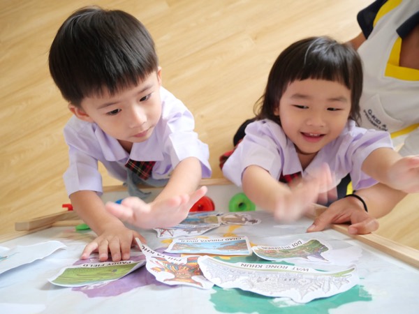 Two children reaching for picture cards of Thai landmarks laid out on the floor