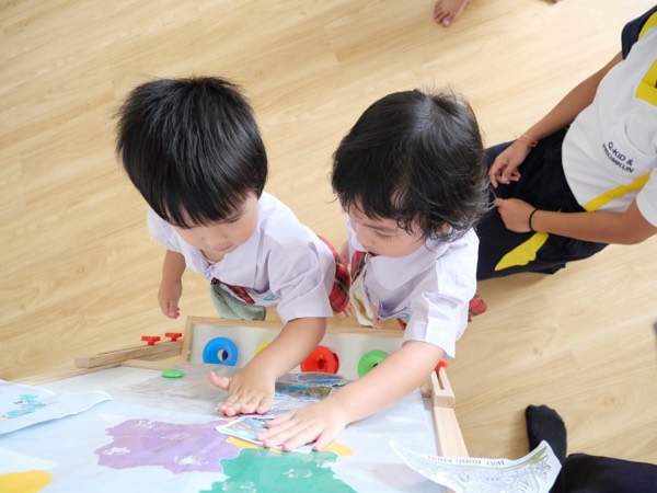 Seen from above, two children pressing pictures onto a painted map with their hands