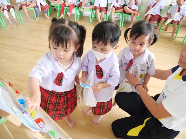 Children waiting their turn beside the easel, a teacher kneeling with them
