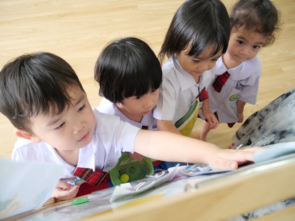Four children reaching across a low table with the painting things on it