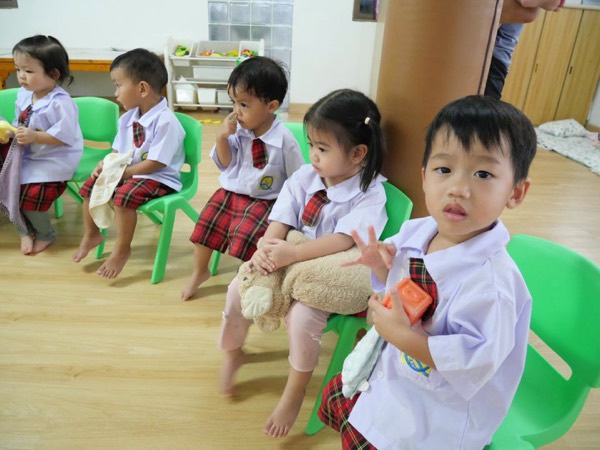 Children sitting in a row, holding soft toys and their favourite things