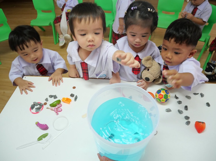 テーブルの上の青い水の容器に石を落とす四人の子ども